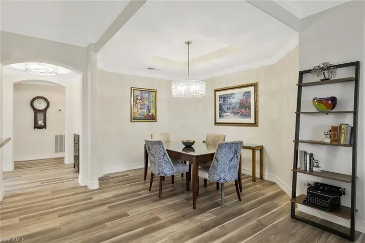 Dining area featuring arched walkways, light wood-style flooring, a raised ceiling, ornamental molding, and a chandelier