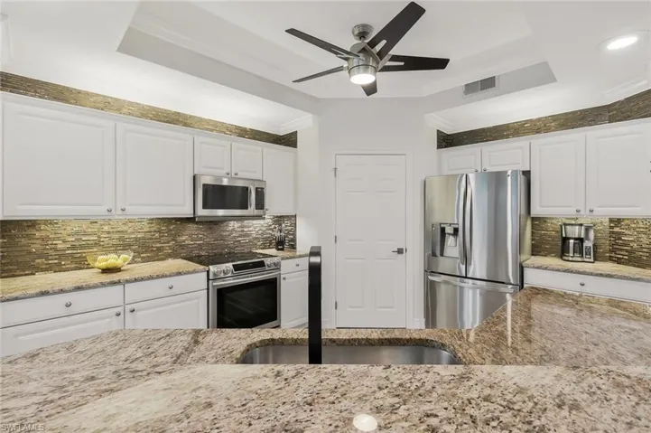 Kitchen featuring white cabinetry, stainless steel appliances, tasteful backsplash, crown molding, and a raised ceiling