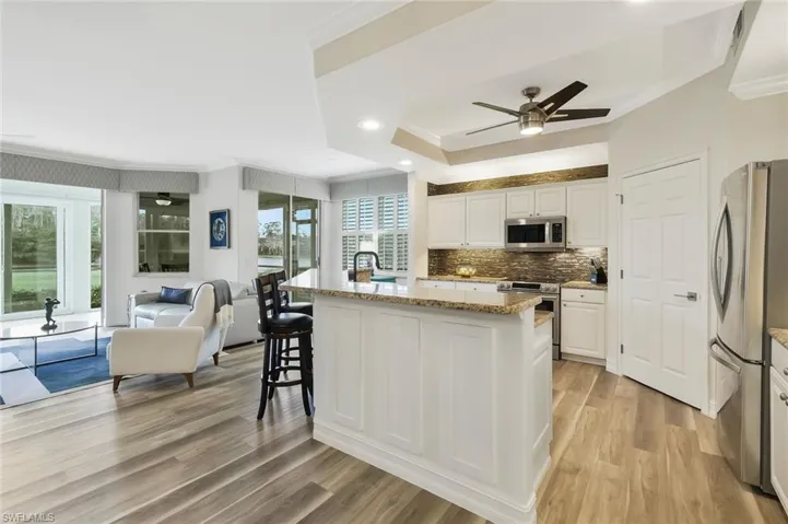 Kitchen with ornamental molding, stainless steel appliances, light stone countertops, a kitchen island, and backsplash