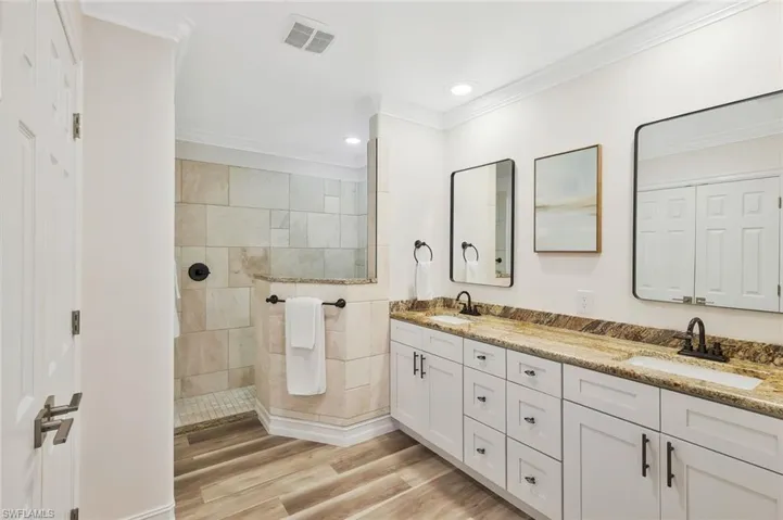 Full bath with double vanity, a walk in shower, light wood-style floors, ornamental molding, and recessed lighting