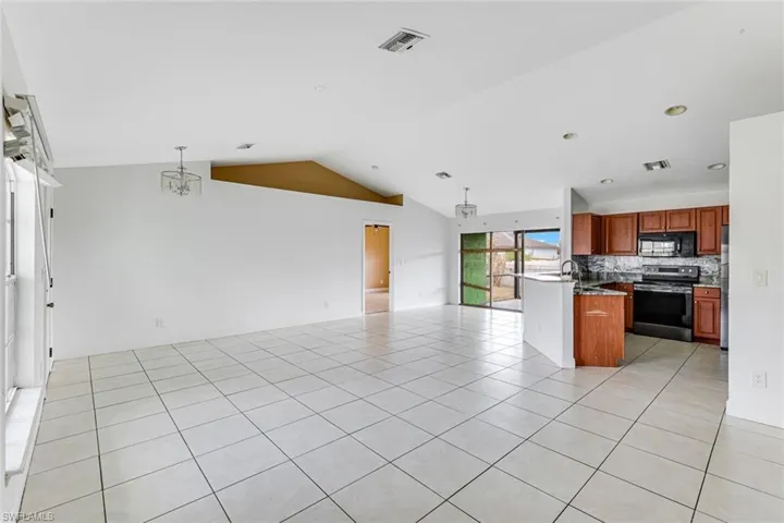 Kitchen with wood finish cabinets, stainless steel electric range oven, open floor plan, tasteful backsplash, and black microwave