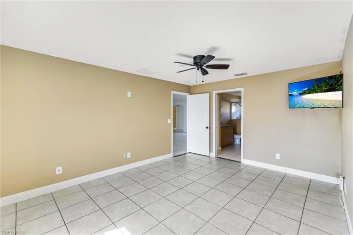 Unfurnished bedroom with ceiling fan, light tile patterned floors, and ensuite bathroom