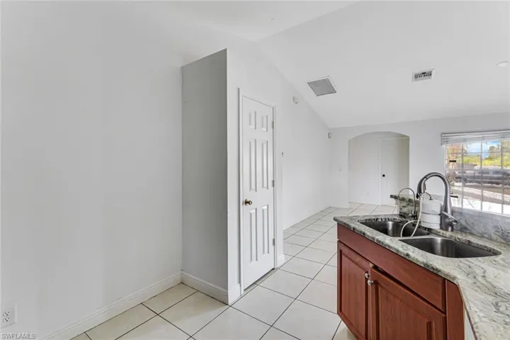 Kitchen featuring arched walkways, light tile patterned floors, lofted ceiling, and light stone countertops
