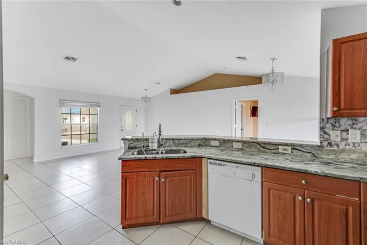 Kitchen with wood finish cabinetry, white dishwasher, light stone countertops, light tile patterned floors, and a peninsula