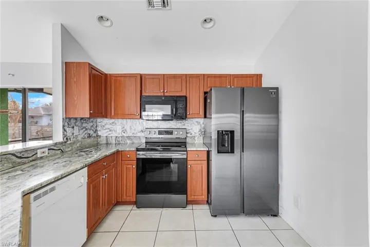 Kitchen with stainless steel appliances, wood finish cabinets, light stone countertops, backsplash, and light tile patterned floors