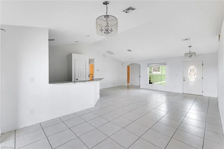 Unfurnished living room featuring hanging lights, arched walkways, light tile patterned flooring, and lofted ceiling