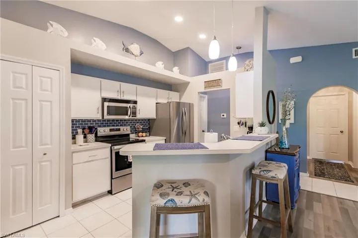 Kitchen featuring stainless steel appliances, hanging light fixtures, light wood-type flooring, kitchen peninsula, and backsplash
