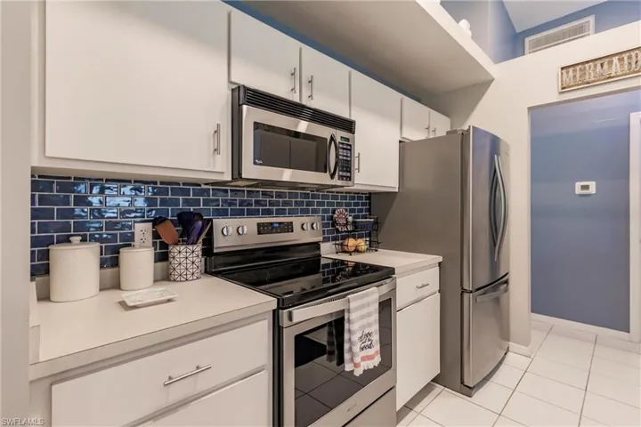 Kitchen with white cabinets, stainless steel appliances, backsplash, and light tile patterned floors