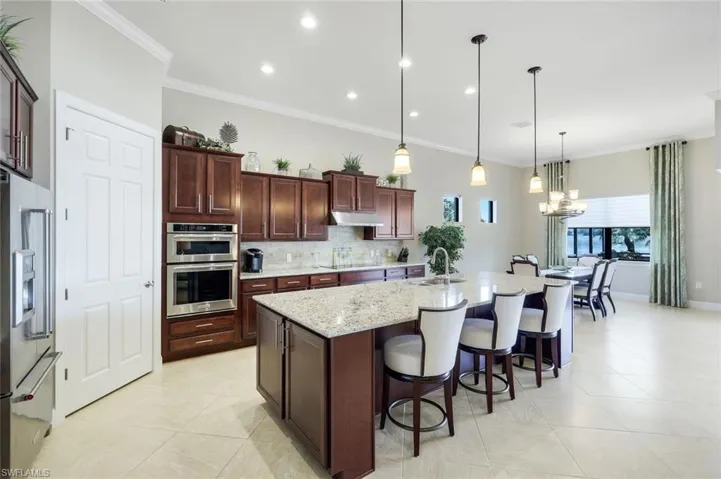 Kitchen featuring a pantry, breakfast bar stainless steel appliances, a center island with sink, crown molding, and light stone countertops