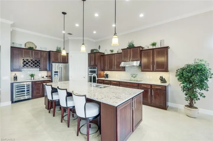 Kitchen with decorative light fixtures, stainless steel appliances, a kitchen breakfast bar, a spacious island, and light stone counters