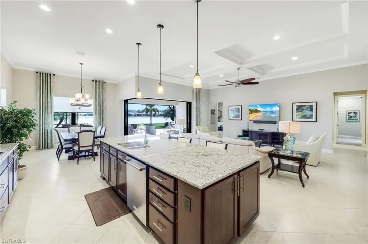 Kitchen with light stone countertops, open floor plan, dark wood finish cabinets, coffered ceiling, and stainless steel dishwasher