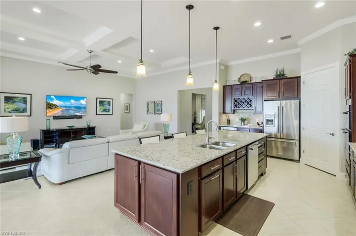 Kitchen featuring an island with sink, light stone counters, coffered ceiling, stainless steel appliances, and ornamental molding