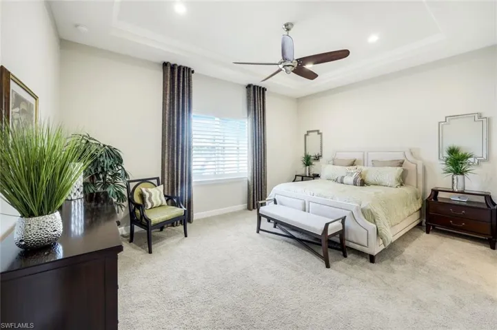 Bedroom with light carpet, ceiling fan, and a raised ceiling