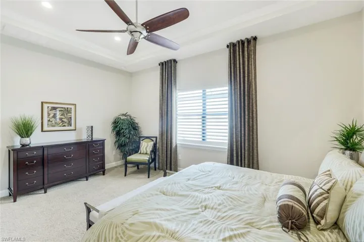 Bedroom with a tray ceiling, light carpet, ceiling fan, and crown molding