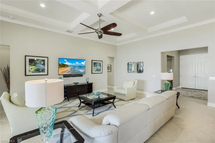 Living room with coffered ceiling, a ceiling fan, ornamental molding, and light tile patterned floors