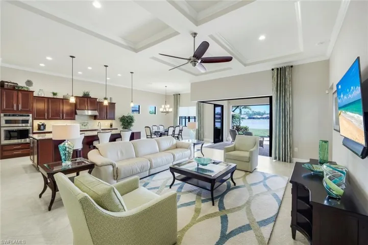 Living room with coffered ceiling, zero corner sliding glass doors, a ceiling fan, hanging lights, crown molding, and light tile patterned floors