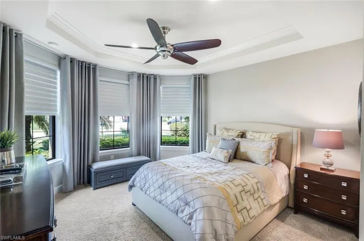 Bedroom with ornamental molding, a ceiling fan, light colored carpet, and a tray ceiling