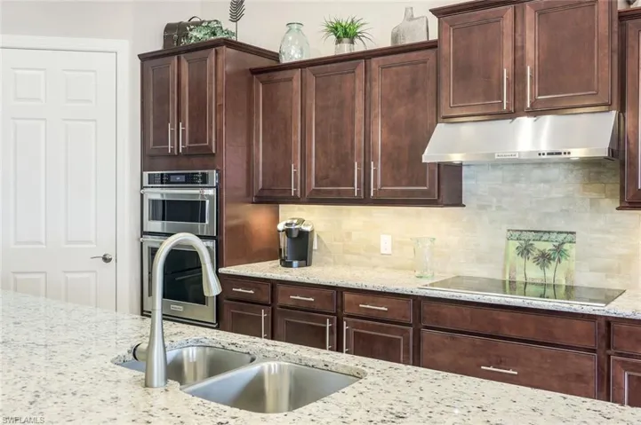 Kitchen with stainless steel double oven, light stone countertops, black electric stovetop, tasteful backsplash, and dark wood finish cabinets