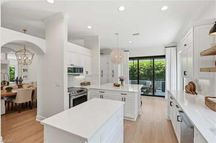 Contemporary kitchen featuring two white islands with light countertops, recessed lighting, wood-finish flooring, a stainless steel oven, and sliding glass doors leading to an outdoor space