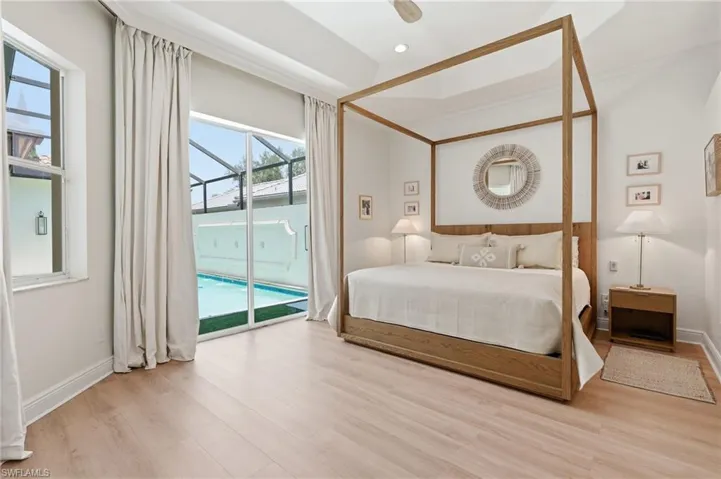 Bedroom featuring wood-finish flooring, a tray ceiling, and direct access to a screened pool area via sliding glass doors