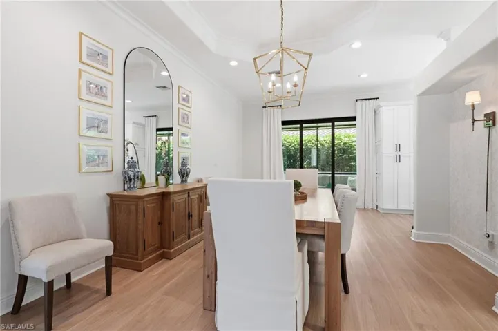 Spacious dining area featuring wood-finish flooring, a tray ceiling with recessed lighting, and a geometric chandelier