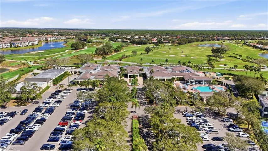 Expansive golf course and clubhouse with a large parking area, surrounding water features, and abundant mature landscaping