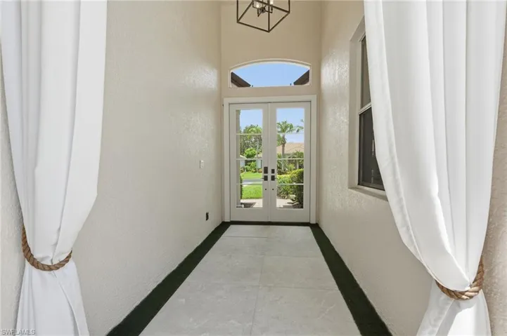 Glass French doors with transom window, vaulted ceiling, tile flooring, and integrated lighting fixture