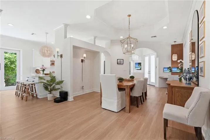 Spacious open-concept living area featuring wood-finish flooring, a tray ceiling with a geometric chandelier, and arched doorways