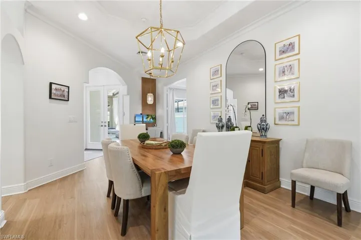 Dining area featuring light wood-finish flooring, a tiered ceiling with recessed lighting, an architectural gold chandelier, and an arched entryway