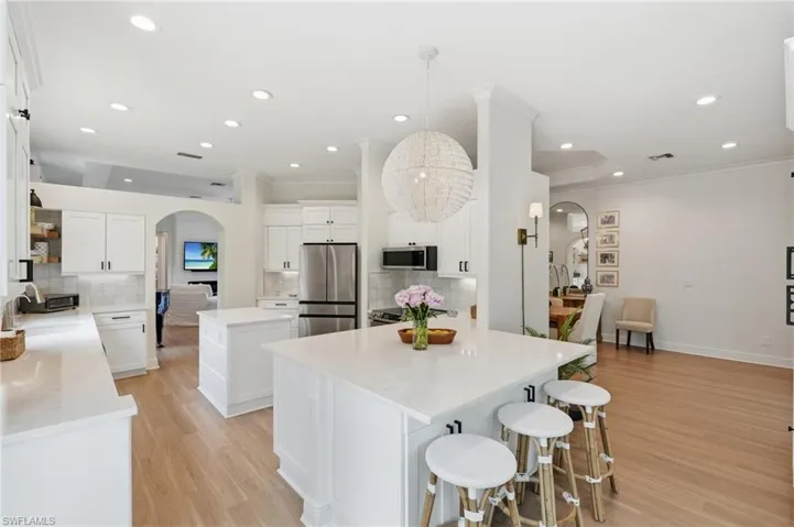 Spacious kitchen featuring two center islands, white cabinetry, integrated stainless steel appliances, wood-finish flooring, and recessed lighting
