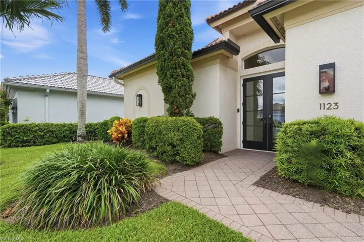 Stucco exterior with a tiled roof, featuring a paver walkway leading to double entry doors with transom window