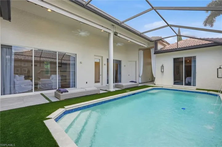 Screened-in pool area featuring a rectangular pool with integrated steps, artificial turf surrounds, and a covered patio with recessed lighting and ceiling fans