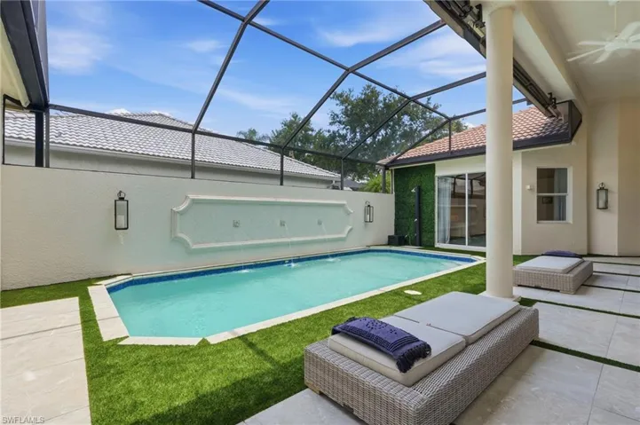 Screened outdoor living area featuring a rectangular pool with a decorative wall fountain, artificial turf, and light-toned patio pavers