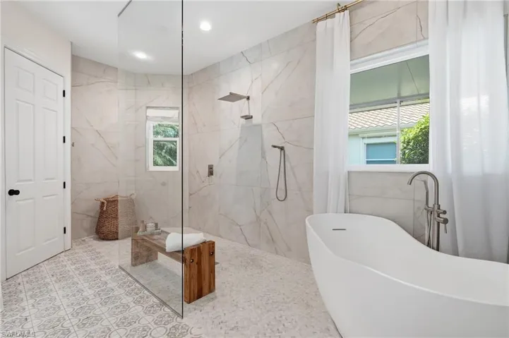 Spacious bathroom featuring a frameless glass shower enclosure, a freestanding soaking tub with a floor-mounted faucet, large format wall tiles, and patterned floor tiles