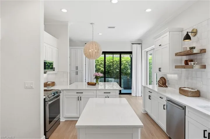 Contemporary kitchen featuring two white islands with solid surface countertops, light wood-finish flooring, white cabinetry with matte black hardware, stainless steel appliances, and a full-height tile backsplash