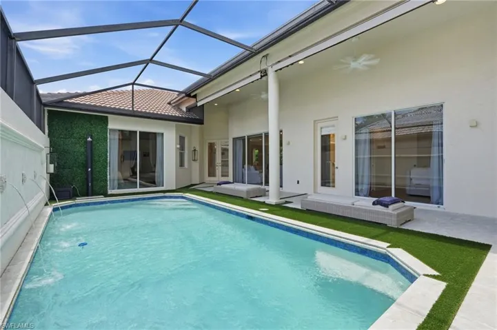 Screened-in outdoor living space featuring a rectangular swimming pool with integrated water features, artificial turf surround, and a covered patio with recessed lighting and ceiling fans