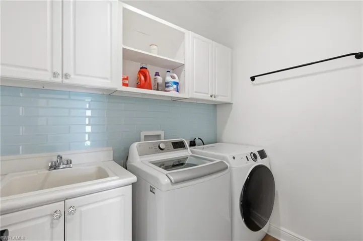 Utility room featuring white cabinetry, a built-in sink with chrome fixtures, light blue subway tile backsplash, and a wall-mounted drying rod