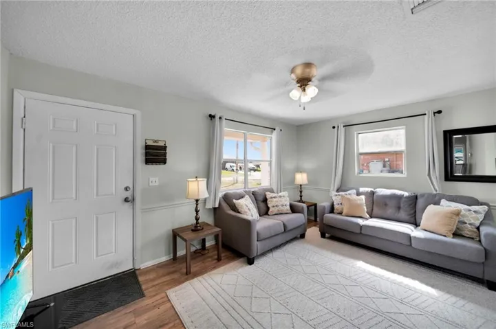 Living area featuring light wood-style flooring, ceiling fan, baseboards, and a textured ceiling