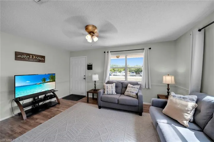 Living room with ceiling fan, baseboards, wood finished floors, and a textured ceiling