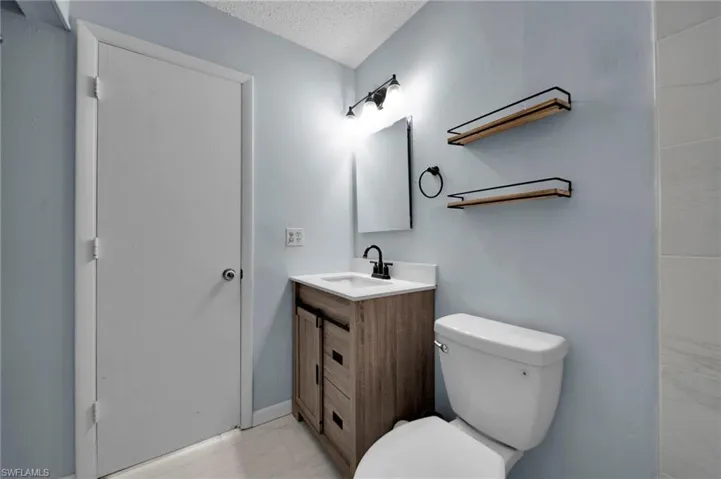 Bathroom with toilet, marble finish floor, vanity, and a textured ceiling
