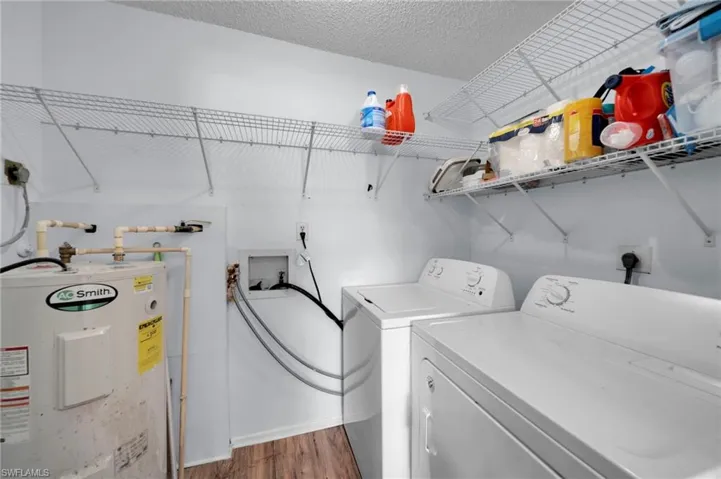 Clothes washing area with water heater, independent washer and dryer, wood finished floors, and laundry area