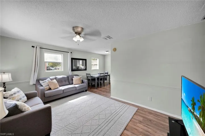 Living room featuring a textured ceiling, wood finished floors, a ceiling fan, and visible vents
