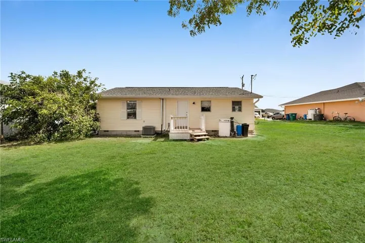 Rear view of house featuring central AC unit, crawl space, and a lawn