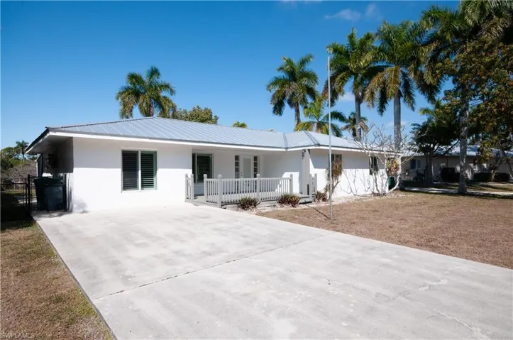 Ranch-style house with stucco siding, a metal roof, a front yard, driveway, and a porch