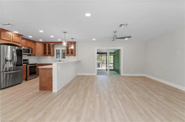 lIVING ROOM OPEN TO Kitchen with stainless steel appliances, glass insert cabinets, wood finish cabinetry, a peninsula, and hanging light fixtures