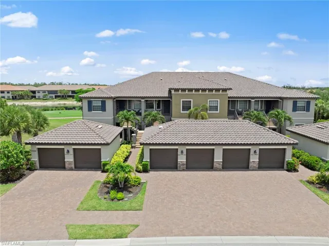 Multi-story stucco exterior featuring a tiled roof, multiple garage bays with paver driveways, and mature tropical landscaping