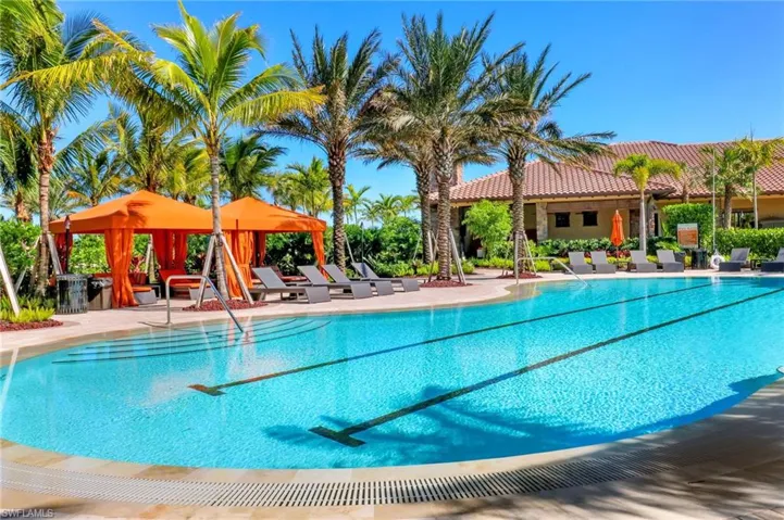 Resort-style pool area featuring a large swimming pool with lap lanes, multiple orange cabanas, numerous lounge chairs, and lush palm trees
