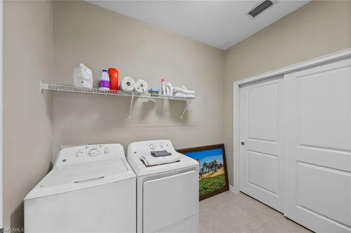 Laundry area featuring light neutral wall paint, tiled flooring, a wire shelving unit, and white sliding closet doors