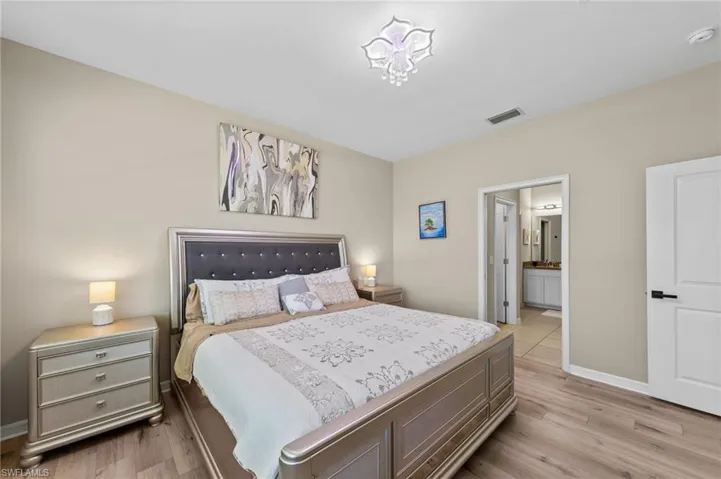 Spacious bedroom featuring wood-finish flooring, a contemporary ceiling light fixture, and neutral wall tones