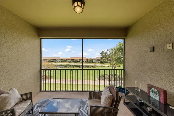 Screened lanai with textured walls, a ceiling-mounted light fixture, and a lake and golf course backdrop